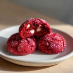 A stack of three vibrant red velvet cake mix cookies, one broken open revealing white chocolate chips inside.