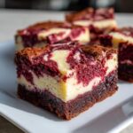 A close-up of a decadent red velvet cheesecake brownies slice showing the marbled red and cream layers over a dark brownie base.