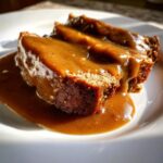 Close-up of thick, rich turkey gravy generously poured over slices of meatloaf on a white plate.