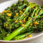 A close-up, vibrant image of perfectly roasted broccolini stalks topped with bright yellow, minced seasoning.