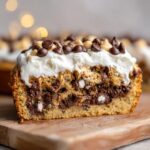 Close-up of a thick slice of cookie cake recipe topped with white frosting and chocolate chips.
