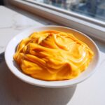 A close-up of thick, vibrant orange nacho cheese sauce swirled beautifully in a small white bowl.