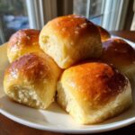 A stack of freshly baked, golden brown, soft dinner rolls glistening with butter.