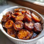 Close-up of rich, glossy southern candied yams coated in dark brown sugar glaze served in a white oval baking dish.