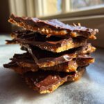 A stack of broken pieces of rich graham cracker toffee topped with shiny melted chocolate.