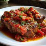 Two pieces of seared steak smothered in chunky tomato sauce and fresh parsley, ready to eat Steak Pizzaiola.