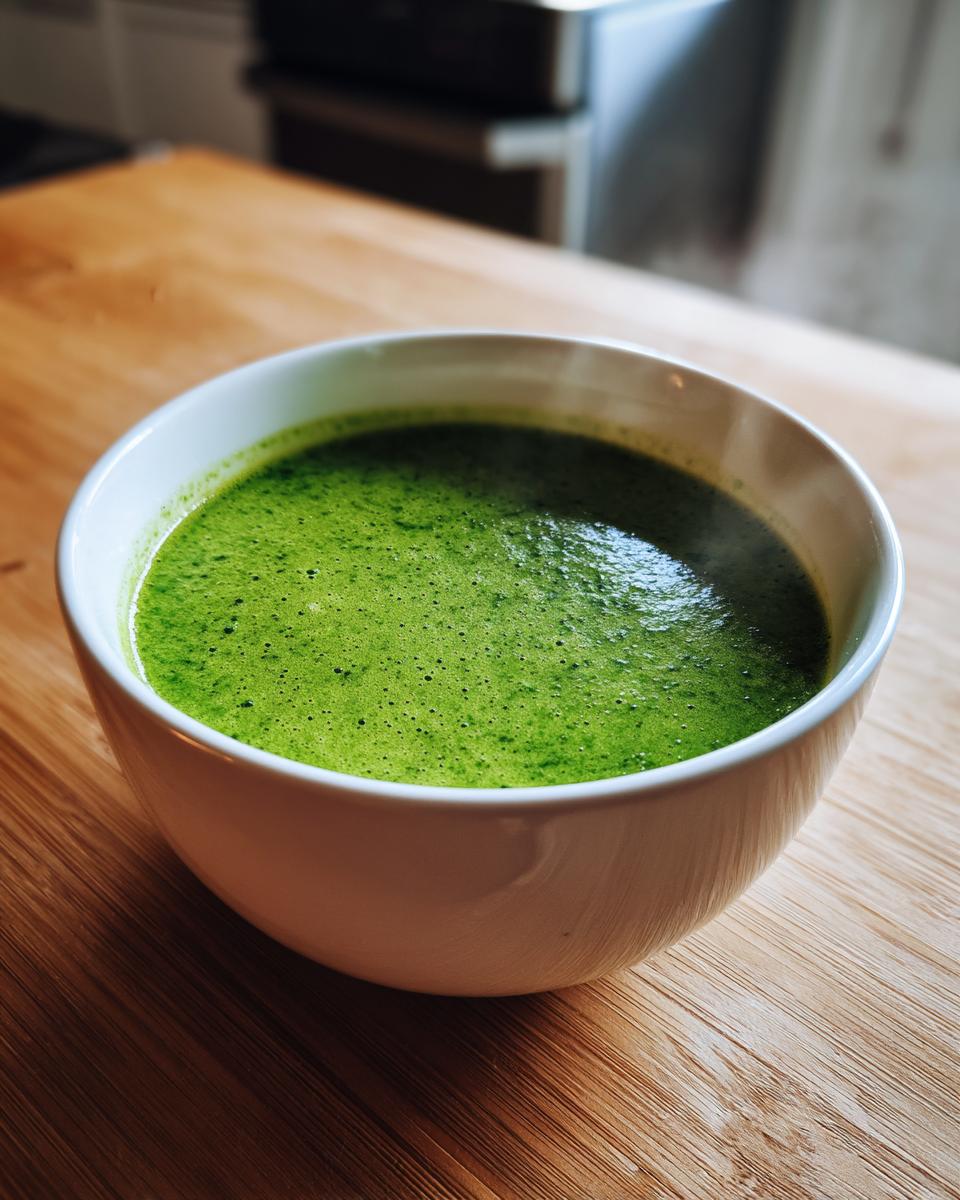 A close-up of a steaming white bowl filled with vibrant green, creamy spinach soup on a wooden table.