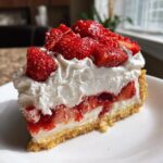 A decadent slice of strawberry shortcake cheesecake topped high with fresh strawberries and whipped cream.