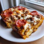 Two thick slices of baked pizza casserole topped with melted cheese, ground meat, and pepperoni slices.