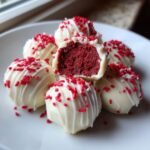 Close-up of white chocolate dipped red velvet cake balls, one cut open revealing the dark red interior.