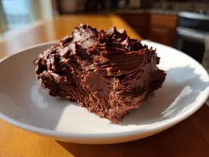 A generous dollop of rich, dark chocolate frosting with textured peaks sitting on a white plate.