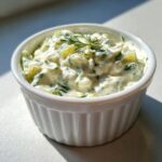 Close-up of creamy, chunky homemade tartar sauce garnished with fresh dill in a white fluted bowl.