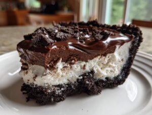 Close-up of a decadent slice of ice cream pie with a dark chocolate crust, white filling, and chocolate topping.