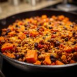 Close-up of a hearty sweet potato skillet topped with melted cheddar cheese, ground meat, black beans, and corn.