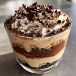 A layered Baileys Chocolate Cheesecake Trifle topped with whipped cream and chocolate chips in a clear glass.