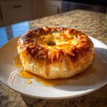 A golden brown baked brie in puff pastry, glistening with honey glaze, served on a white plate.
