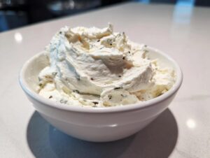 A close-up of thick, creamy blue cheese dip swirled high in a small white bowl on a light countertop.