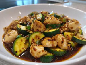 Close-up of tender chicken pieces and sliced zucchini coated in a dark, savory sauce in a white bowl, showcasing the chicken zucchini stir fry.