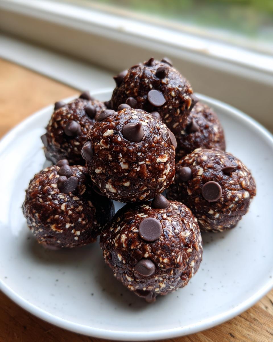 A close-up of several rich, dark chocolate chip protein balls stacked on a light speckled plate.