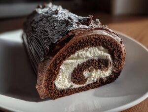 Cross-section of a rich chocolate yule log cake showing a swirl of white cream filling, dusted with powdered sugar.