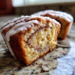 Close-up of a cinnamon roll muffin cut in half showing the swirl and white icing drizzle.