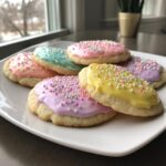 A plate of sugar cookies topped with brightly colored, hard-set sugar cookie icing and sprinkles.