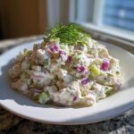 A mound of creamy cottage cheese chicken salad mixed with diced red onion and celery, topped with fresh dill.