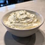 Close-up of creamy, white blue cheese dip with visible dark specks, served in a white bowl.