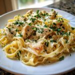 A close-up of creamy chicken fettuccine alfredo pasta topped with fresh parsley and Parmesan cheese.