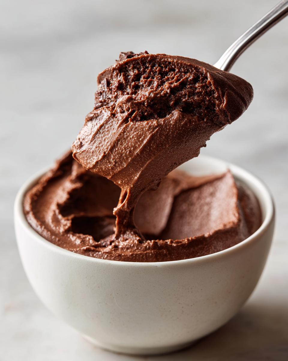 A spoonful of rich, creamy chocolate pudding being lifted from a white bowl.