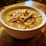 A close-up of a creamy bowl of crockpot white chicken chili topped with shredded chicken, white beans, and corn.