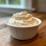 A close-up of thick, creamy horseradish sauce mounded high in a small white fluted ramekin.