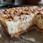 A close-up cross-section of a creamy Million Dollar Pie showing the graham cracker crust, filling with fruit pieces, and a pecan topping.