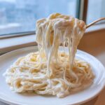 A fork lifting fettuccine coated in thick, creamy olive garden alfredo sauce, showing a delicious cheese pull.