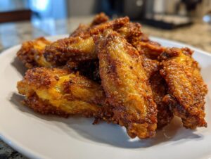 A close-up of several golden brown, seasoned crispy air fryer chicken wings piled on a white plate.