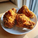 Four pieces of golden brown, crispy air fryer fried chicken arranged on a white plate.