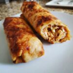 Two golden-brown, crispy Chimichangas on a white plate, one cut open showing shredded chicken and melted cheese filling.