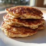 Close-up of a stack of four fluffy banana pancakes with golden-brown, caramelized edges.