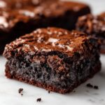 A close-up, decadent square of fudgy oreo brownies showing a shiny, crackled top and dense interior.