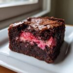 Close-up of a fudgy square of strawberry brownies showing a bright pink, fruity swirl filling inside the dark chocolate base.