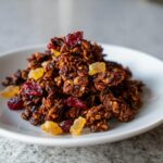 A mound of dark, rich gingerbread granola mixed with dried cranberries and candied ginger pieces.