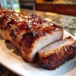 Close-up of a sliced, glazed pork tenderloin recipe showing juicy white meat and a dark, caramelized exterior.