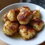 Close-up of several golden brown, pan-fried potato dumplings seasoned with herbs, resting in a white bowl.