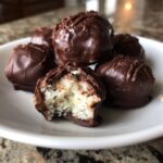 A plate of homemade almond joy truffles, one bitten open to show the shredded coconut center.
