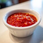 Close-up of vibrant, chunky homemade cocktail sauce served in a small white ramekin.