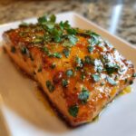 Close-up of a perfectly cooked honey garlic salmon recipe fillet, glistening with glaze and topped with fresh chopped parsley.
