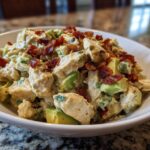 A close-up of creamy honey mustard chicken salad mixed with chunks of avocado and topped with crispy bacon bits.