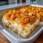 A close-up of a creamy slice of hot chicken salad casserole topped with crunchy, golden corn flakes.