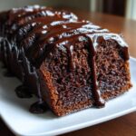 Close-up of a slice of rich, moist hot fudge brownie bread topped with glossy, dripping chocolate sauce.