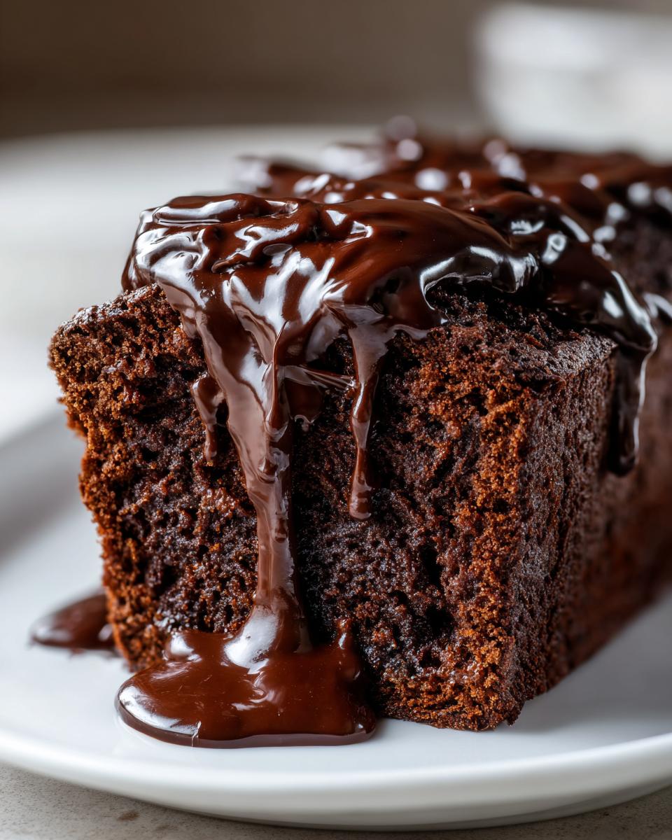 Close-up of a slice of moist hot fudge brownie bread topped with thick, glossy chocolate fudge sauce dripping down the side.